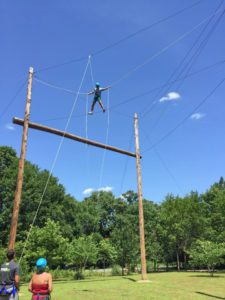 A man hanging from the side of an obstacle course.