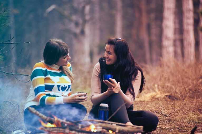 Two women sitting on the ground near a fire.